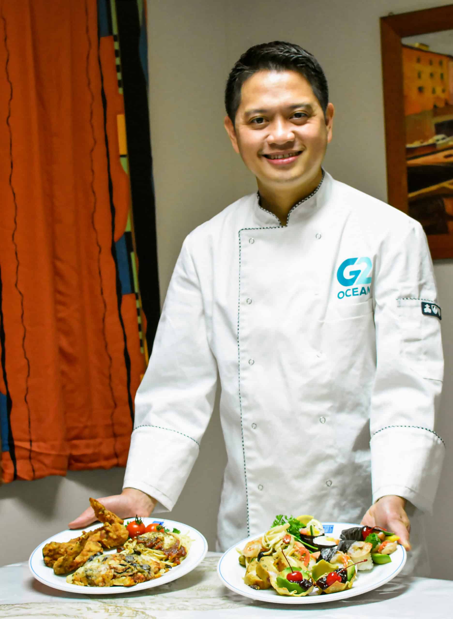 Filipino employee with two plates of food. Employee in G2 Ocean uniform working as Chief Cook.